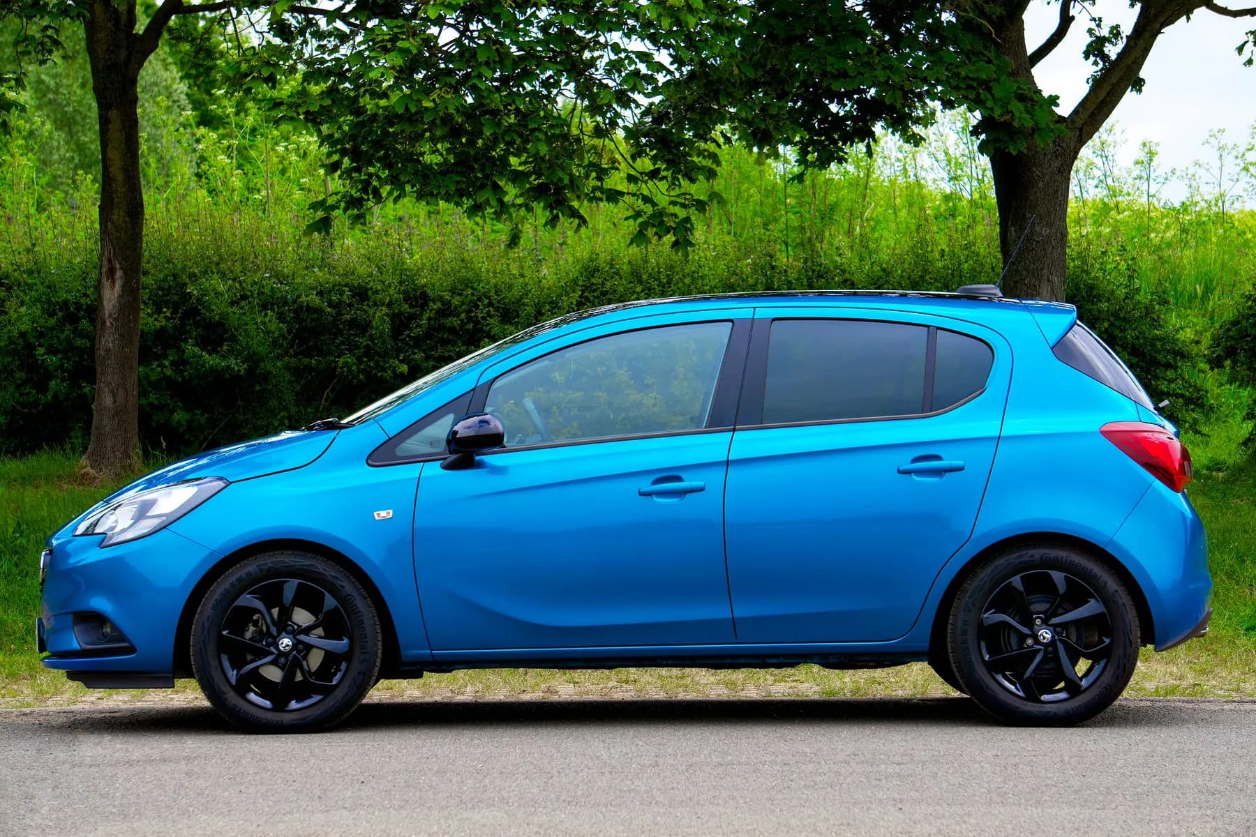 Opel Corsa azul de perfil, en una carretera arbolada