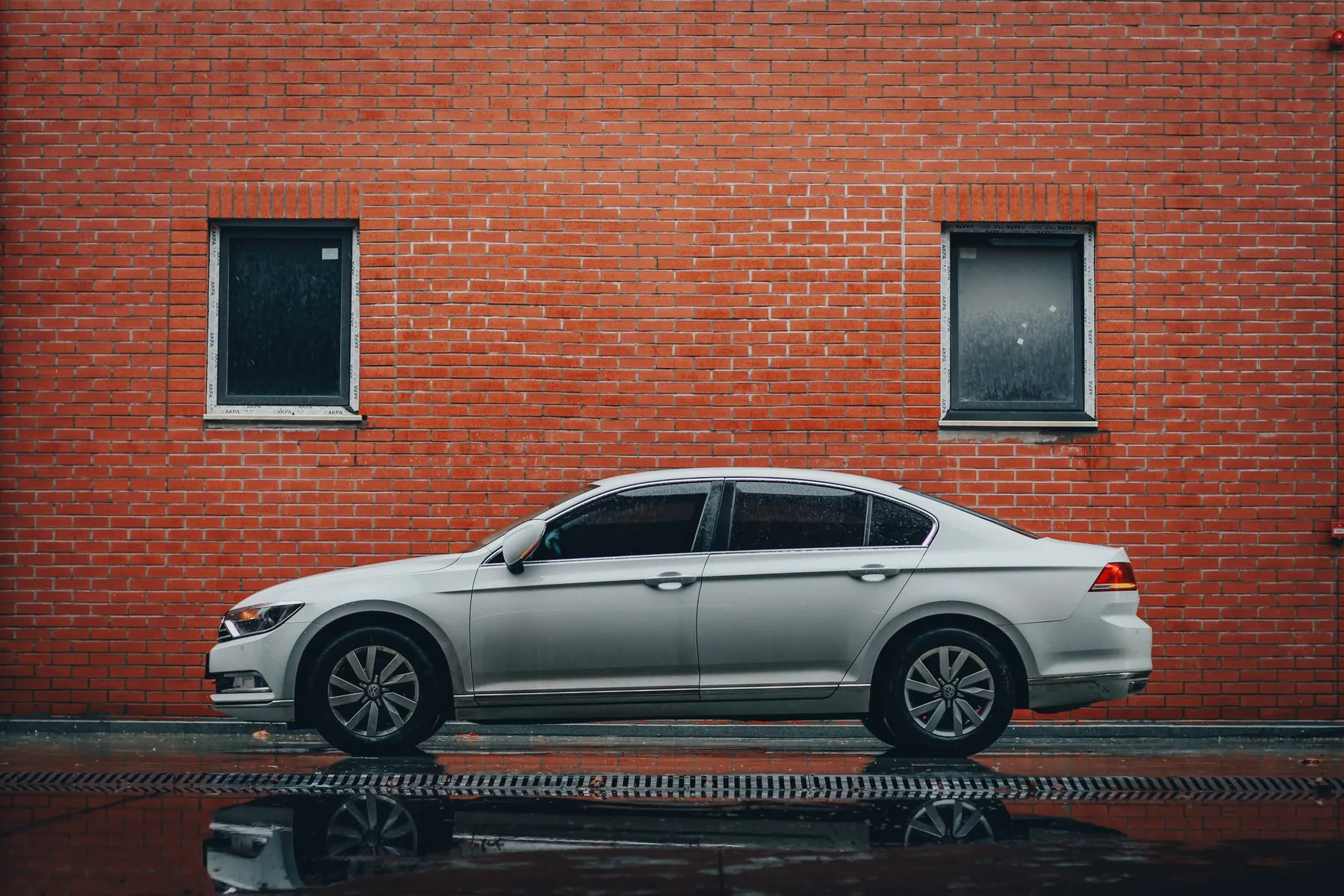 Volkswagen Passat plateado de perfil, contra una pared de ladrillo