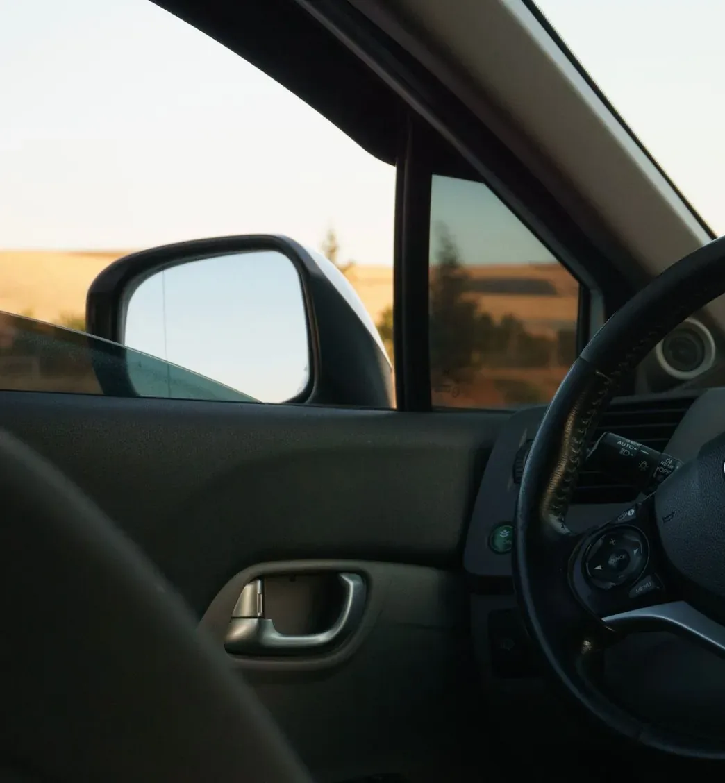 Interior de un coche desde el asiento del conductor, con la ventanilla bajada y el campo al fondo